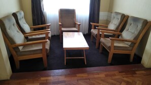A room with a wooden herringbone floor, a central table, and four upholstered armchairs. - Kenmosa Resort (Eldoret)