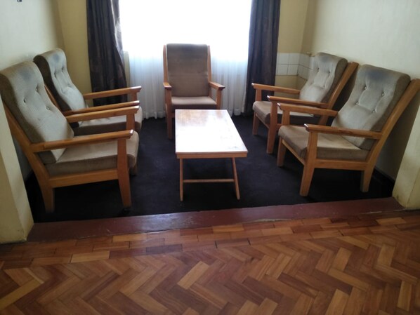 Een kamer met een houten visgraatvloer, een centrale tafel en vier gestoffeerde fauteuils.