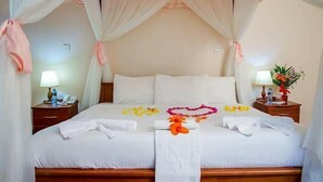 A neatly made bed with a canopy, a bedside table with a lamp, and a small plant on the nightstand. - Kenmosa Resort (Eldoret)
