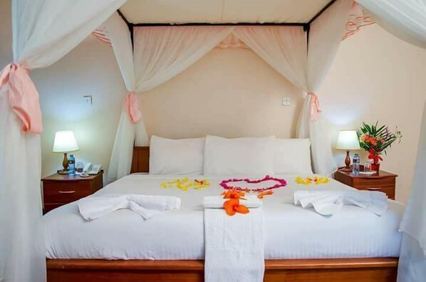 A neatly made bed with a canopy, a bedside table with a lamp, and a small plant on the nightstand. - Kenmosa Resort (Eldoret)