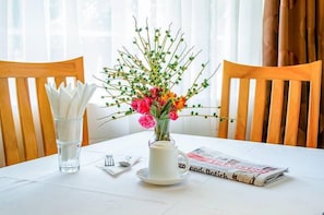 Ett bord dukat med en vas med blommor, ett glas vatten, bestick och en tidning.
