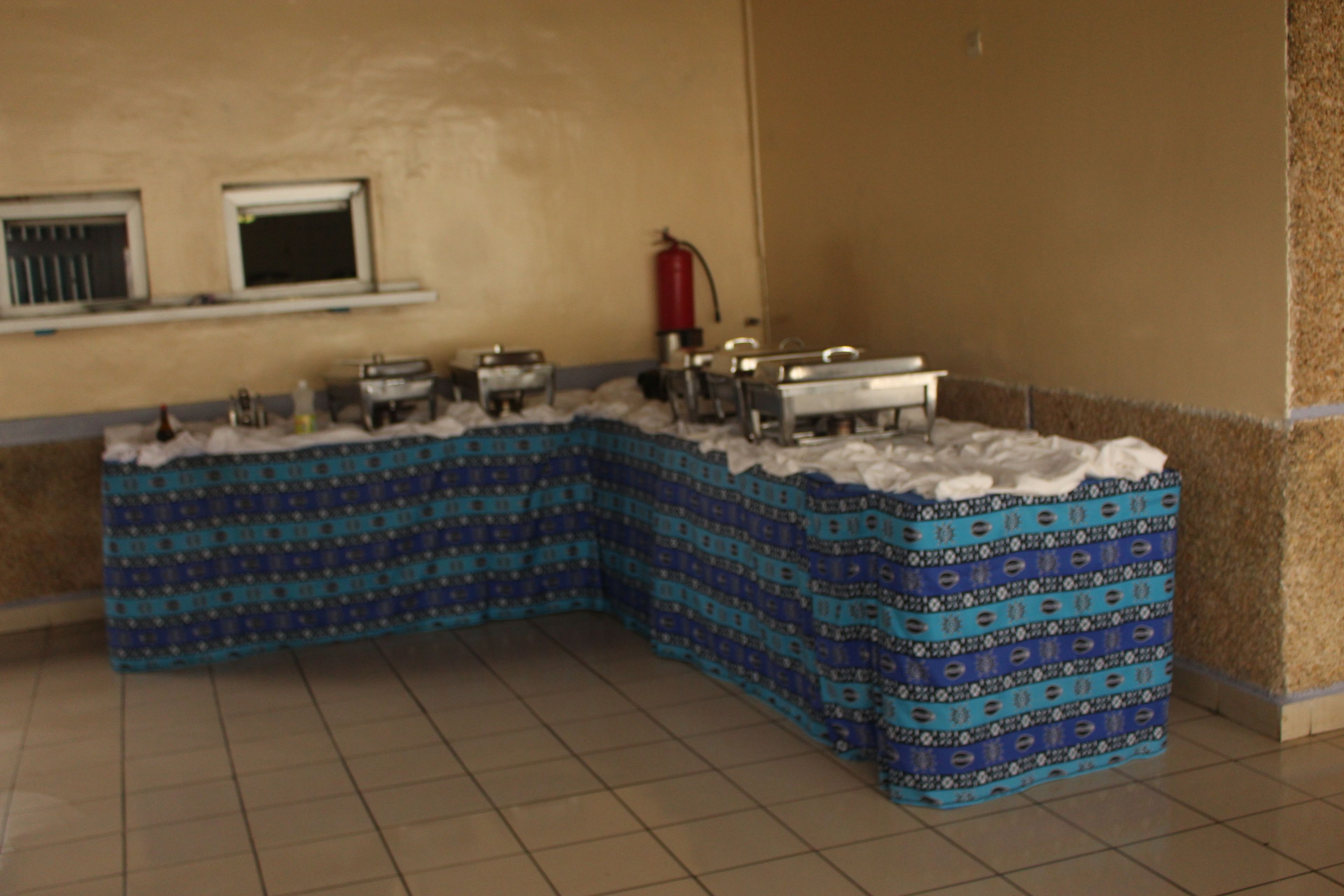 A corner buffet setup with a patterned blue and white tablecloth, a fire extinguisher, and a window above the counter.