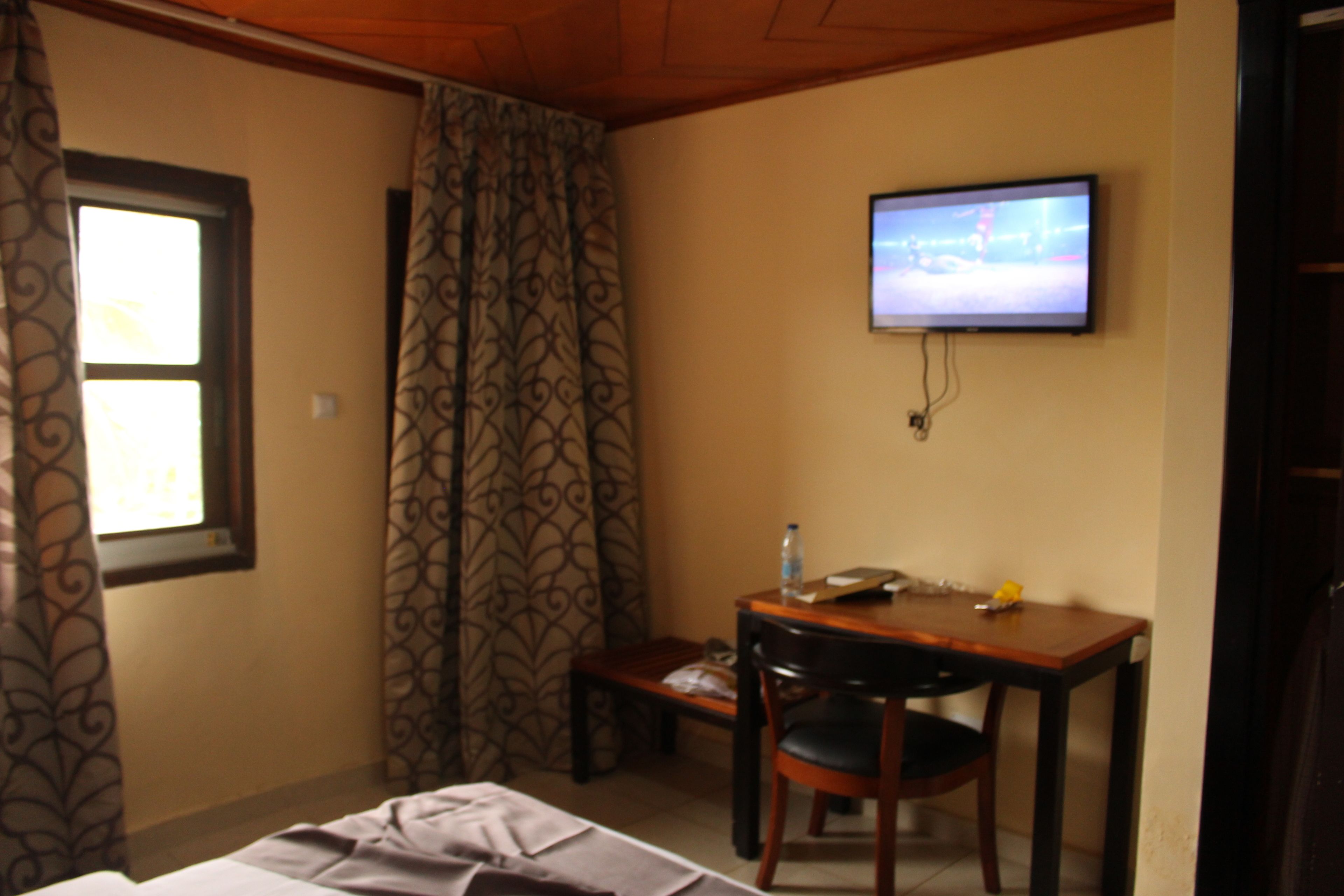A hotel room with a bed, a desk with a chair, a television mounted on the wall, and patterned curtains.
