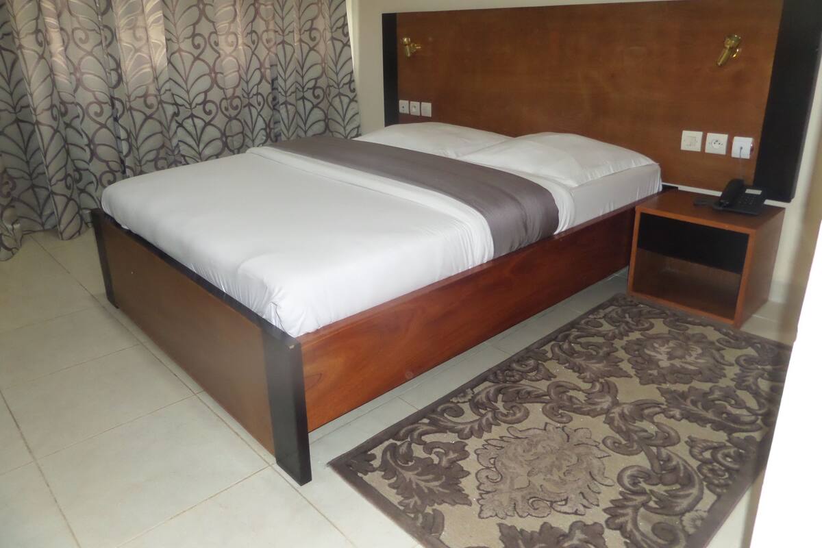 A bedroom with a wooden bed, a bedside table with a phone, and a patterned rug.