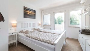 Un dormitorio con cama blanca, mesitas de noche y una ventana con persianas.