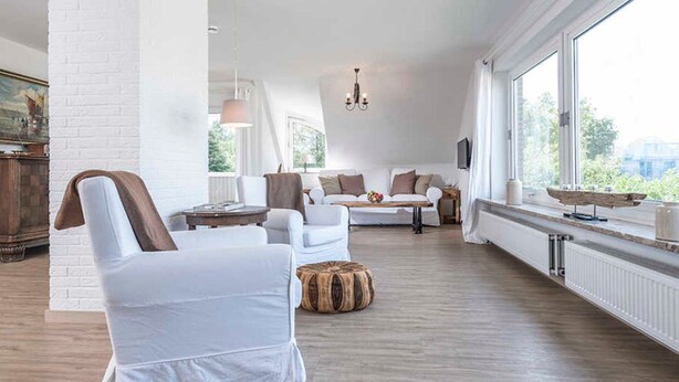 Un salón amplio con un sofá blanco, una mesa de centro de madera y un ventanal con vistas a zonas verdes.