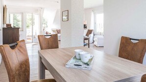 Un comedor con mesa de madera y sillas de cuero, una bandeja con tazas, y vista a un balcón con mobiliario exterior.