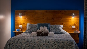 Un lit bien fait, recouvert d’une couvre-lit à motifs floraux, un panier rempli de serviettes et deux lampes de chevet pos ées sur des tables de nuit en bois.