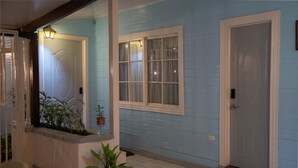 Un couloir avec une porte bleue, une fenêtre à cadre blanc et des plantes en pot.