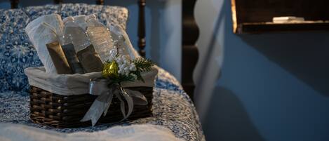 A bed with a blue and white patterned bedspread, a wicker basket with toiletries, and a small bouquet of flowers.