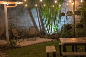 An outdoor patio area with a stone wall, bamboo plants, a wooden table, and chairs. - Alice y Juancito Boutique Hotel (Alajuela)