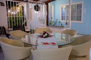 A round glass table with wicker chairs, a white tablecloth with a 'Happy Holidays' message, and a decorative wreath on a white door. - Alice y Juancito Boutique Hotel (Alajuela)