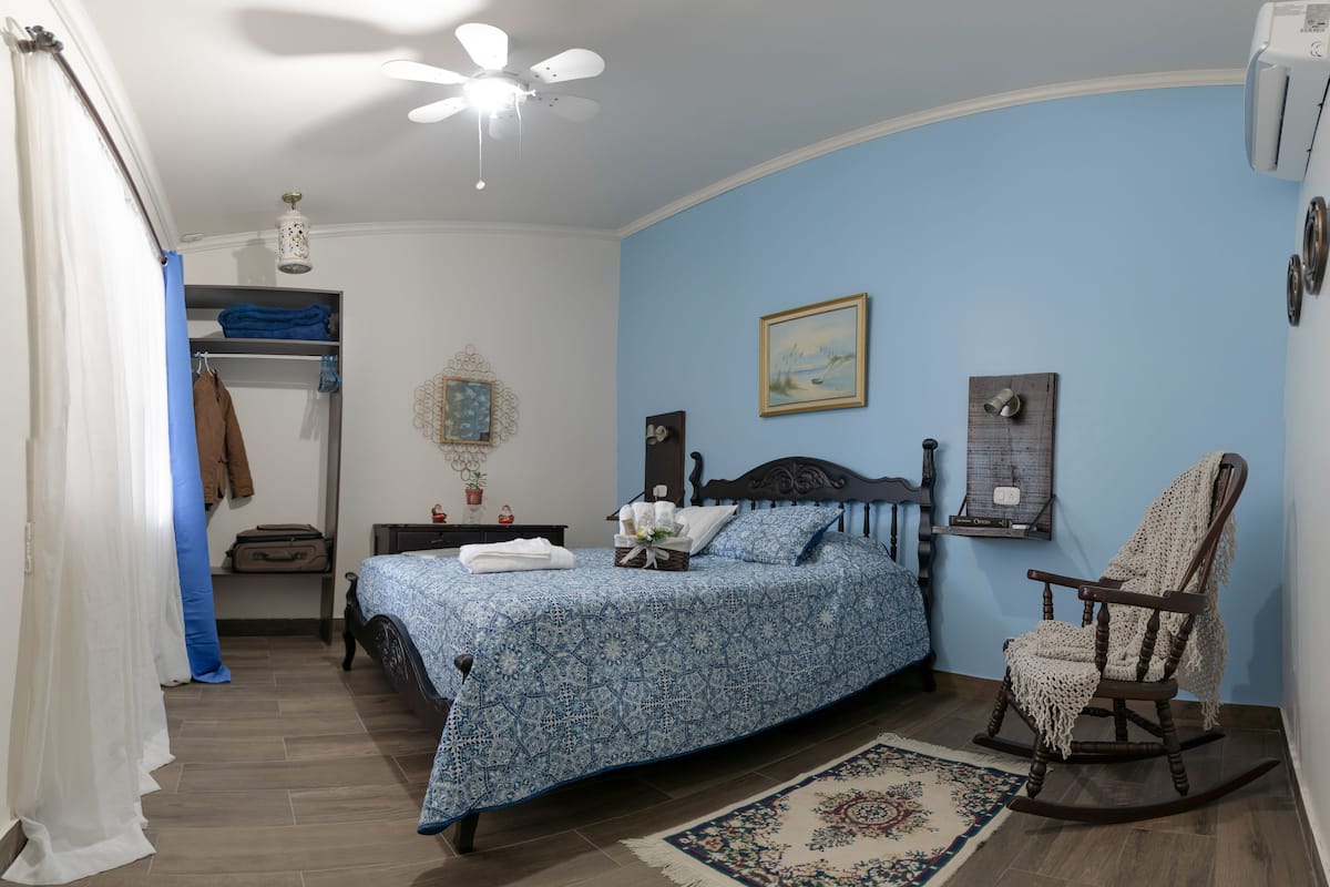 Un dormitorio con cama, una mecedora, una mesita de noche, un armario y un ventilador de techo.