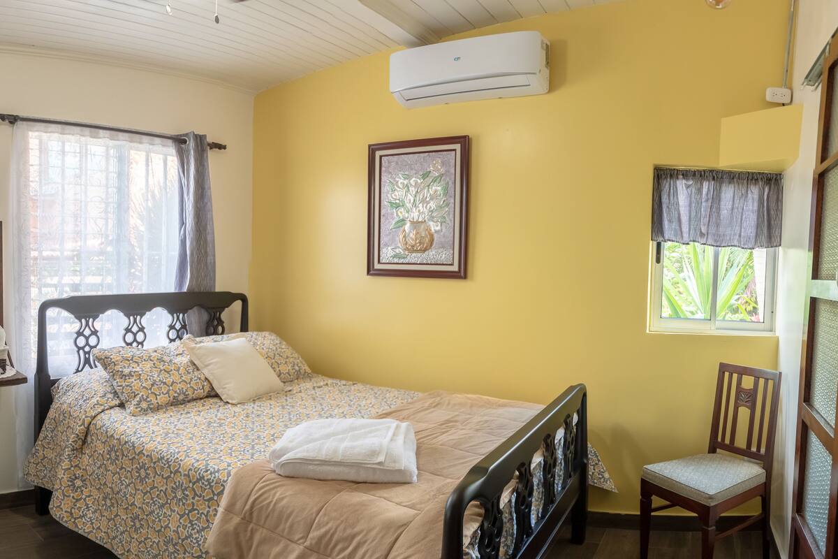 Un dormitorio con cama, una silla, una mesita de noche y una ventana con cortinas.