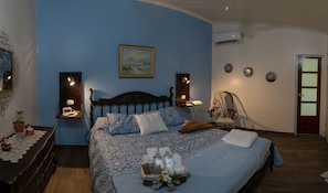 A bedroom with a bed, bedside lamps, a nightstand, a chair, a wall-mounted air conditioner, and a door. - Alice y Juancito Boutique Hotel (Alajuela)