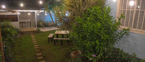A patio area with a wooden deck, a table, and chairs. There are potted plants and a string of lights.