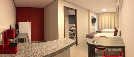 A compact hotel room with a kitchenette, a dining area, and a bed.