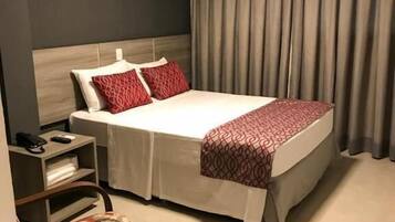 Una habitación de hotel con cama, mesita de noche, una silla y ventana con cortinas.