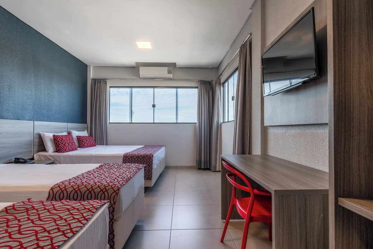 A hotel room with two beds, a desk, a TV, and a window with curtains.