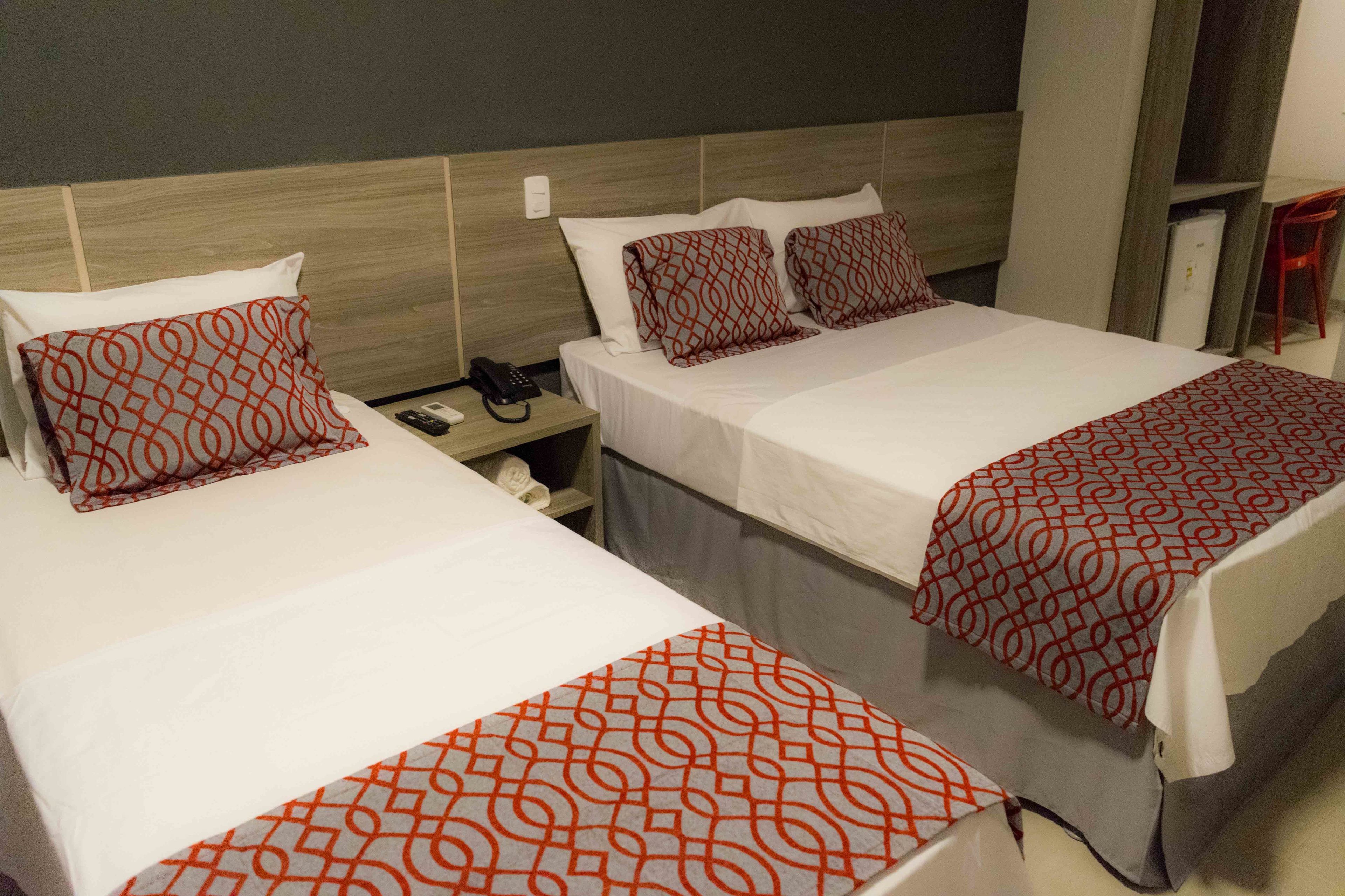 Two twin beds with matching red and white patterned bedspreads, a bedside table with a phone, and a small nightstand with a lamp.