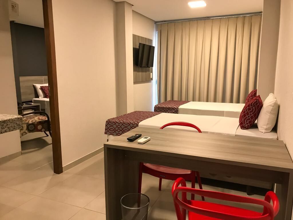 A compact hotel room with a bed, a desk, and a chair. A television is mounted on the wall, and there is a window with curtains.