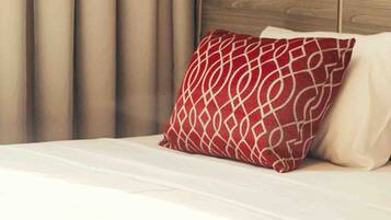 Una cama bien hecha con una colcha estampada, un cojín rojo y blanco, y un cabecero de madera.