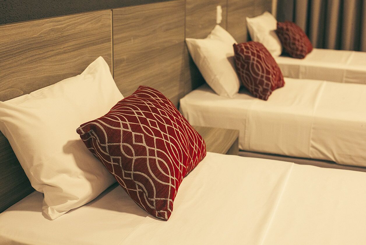 Habitación de hotel con dos camas, cada una con ropa de cama blanca y almohadas rojas estampadas.