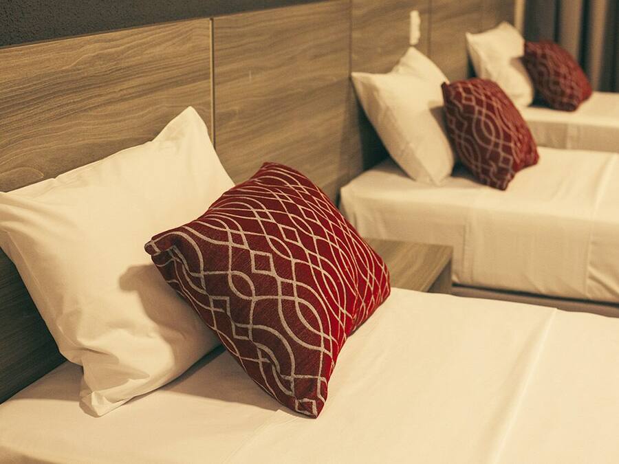 Habitación de hotel con dos camas, cada una con ropa de cama blanca y almohadas rojas estampadas.