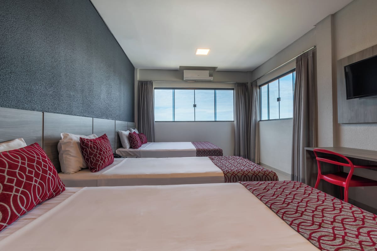 A hotel room with two beds, a desk, a TV, and large windows.