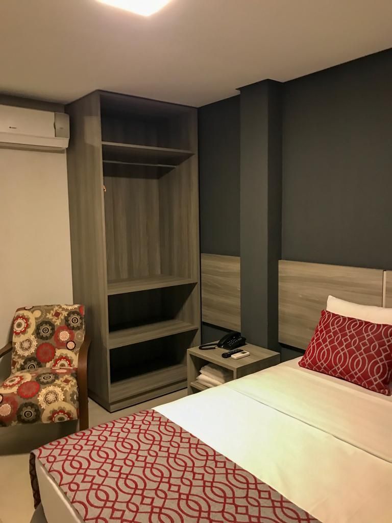 Una habitación de hotel con una cama, una silla, un armario y una mesita de noche.