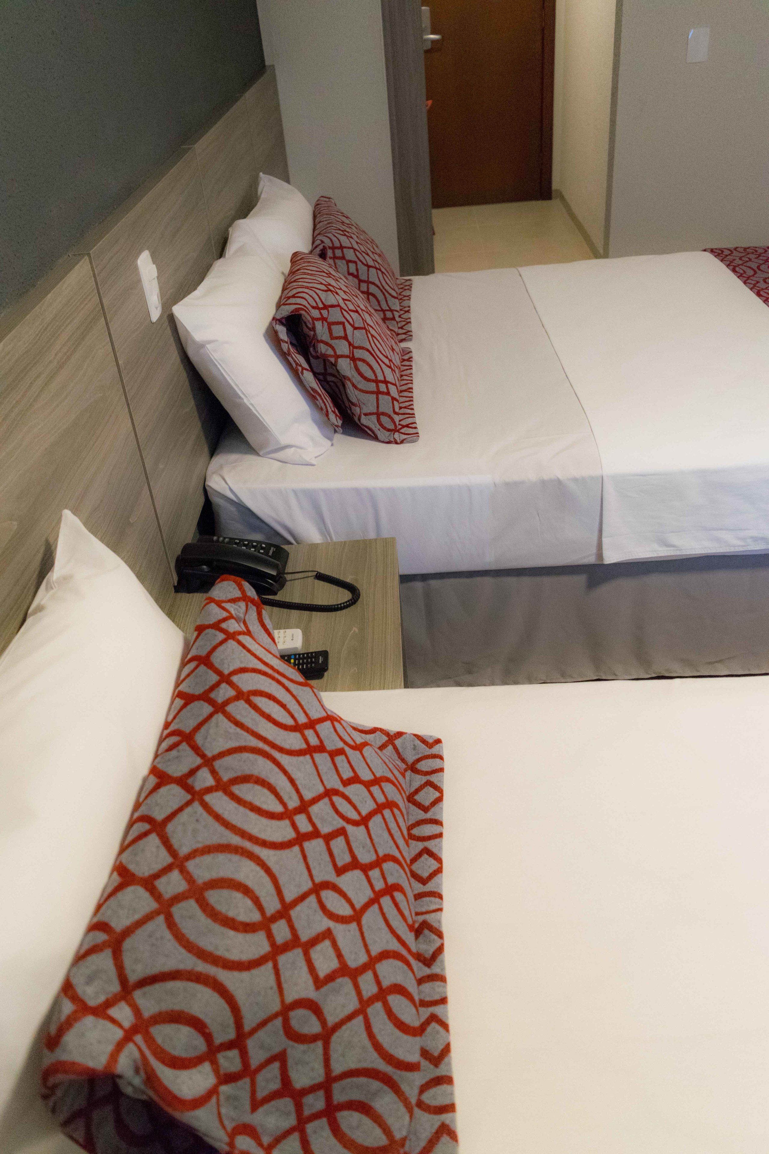 Two single beds with white linens and red patterned pillows. A black telephone is placed on the nightstand between the beds.