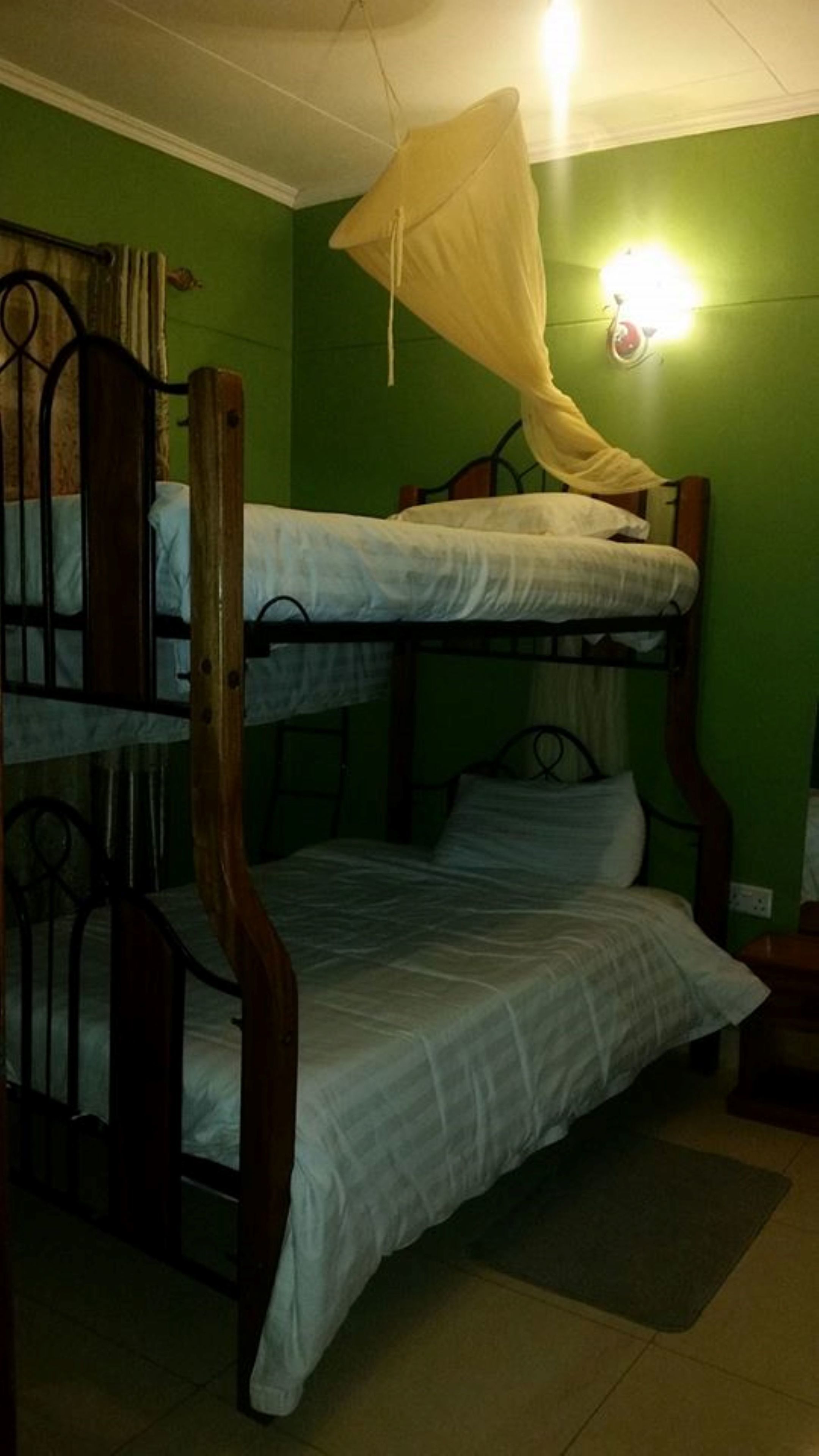 A bunk bed room with green walls, a mosquito net, and a small bedside table.