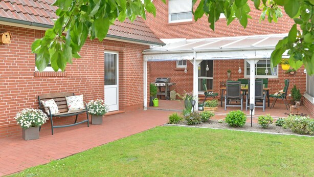A brick house with a patio, a covered outdoor seating area, and a lawn. - Apartment - Apartment Sonnenberg, 25502 (Weener)