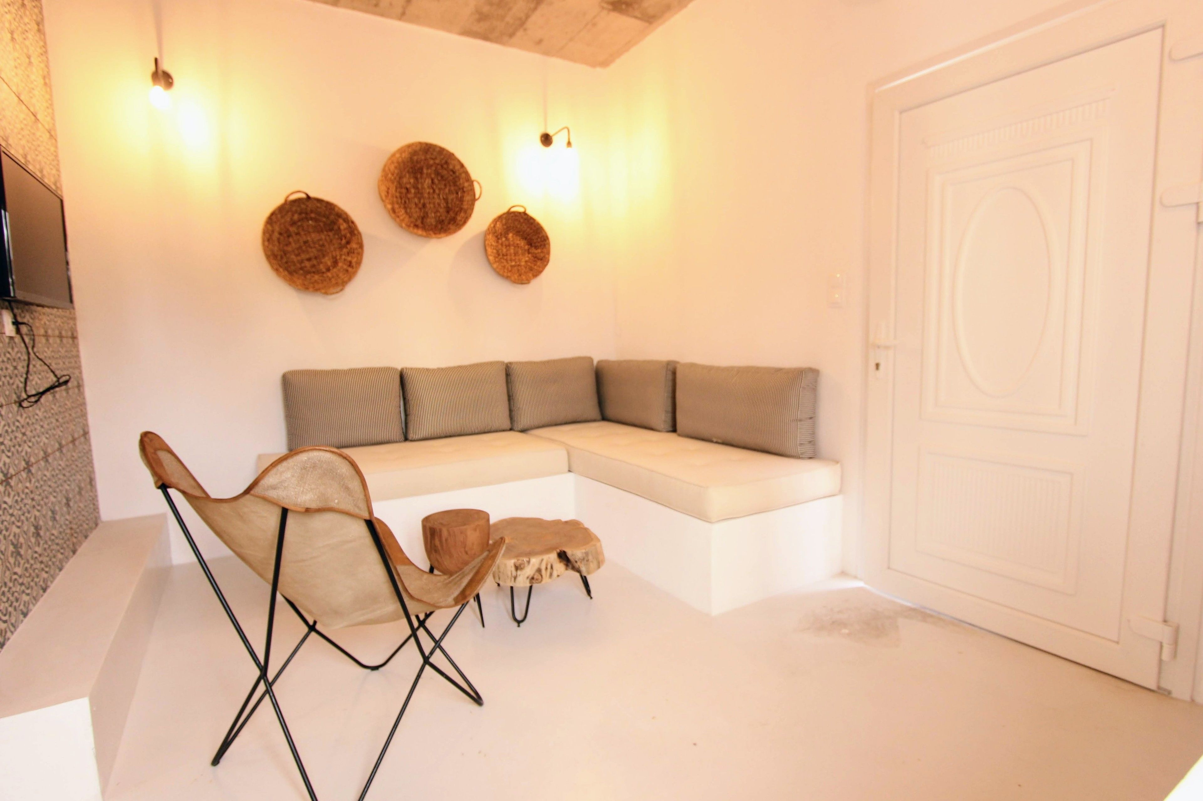 A modern living room with a sectional sofa, two leather chairs, and a small wooden table. There are three wall-mounted lights and a flat-screen TV mounted on the wall.