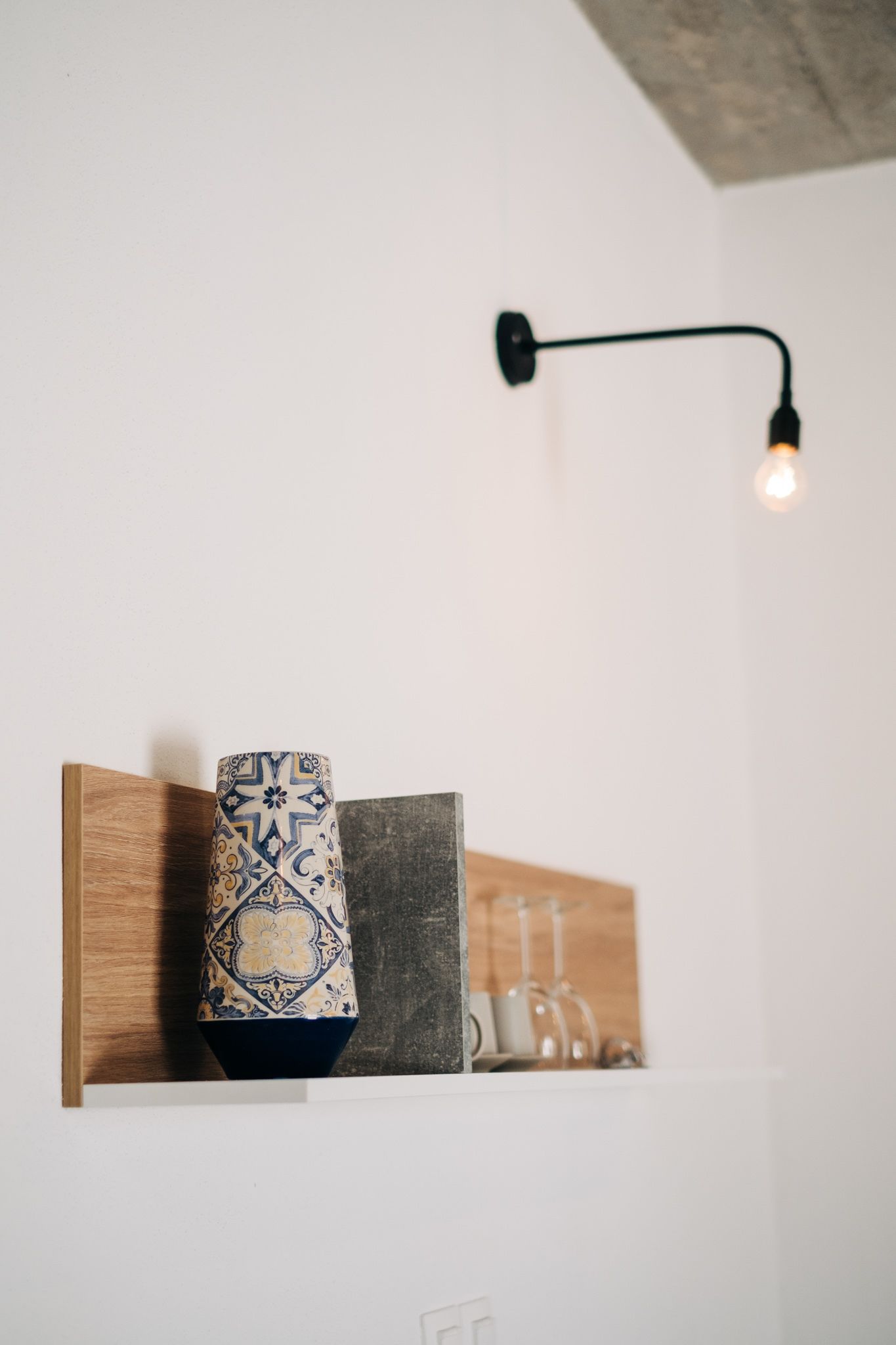 A shelf with a patterned vase, a candle holder, and a wine glass.