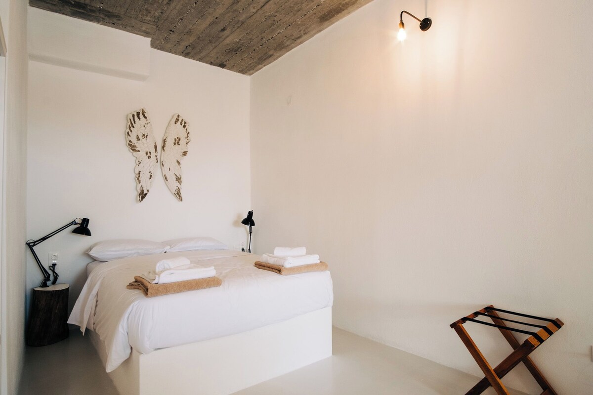 A minimalist bedroom with a bed, two bedside lamps, a wooden floor, and a wooden headboard.