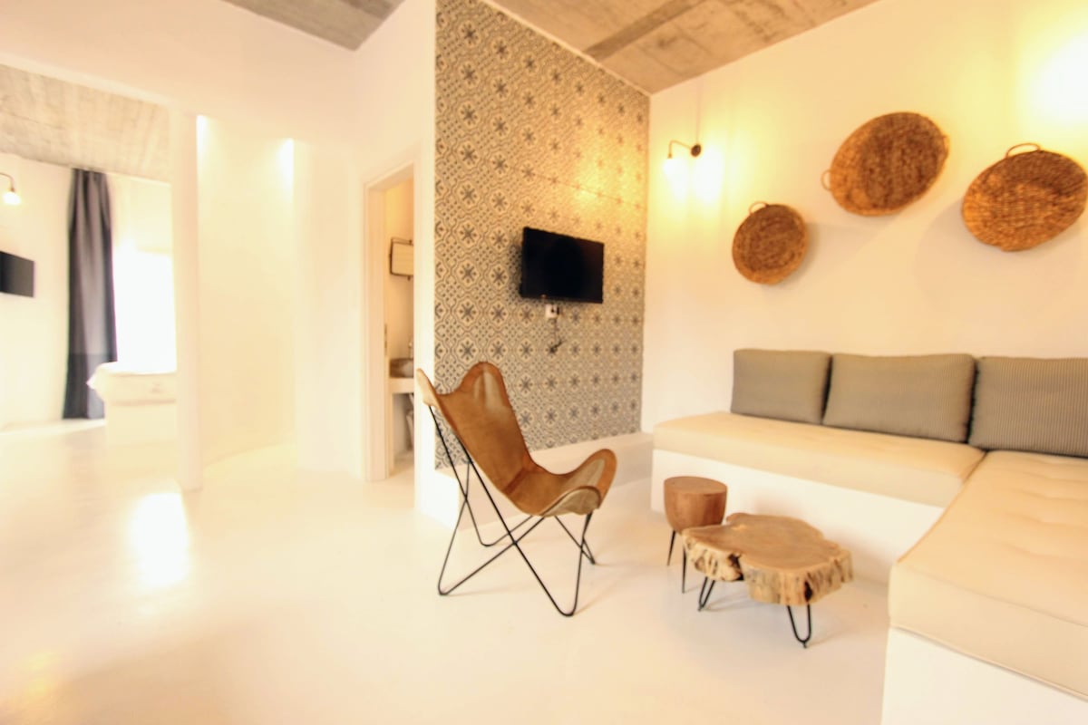 A modern living room with a white sofa, a leather chair, and a round wooden coffee table.