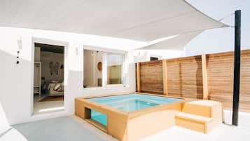Un área de piscina moderna al aire libre con cubierta de madera, cerramiento de vidrio y una sombrilla grande que proporciona sombra.