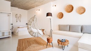 A modern living room with a hanging chair, a floor lamp, a sofa, and a coffee table. - Mesanto Luxury Suites (Santorini)
