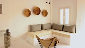 A modern living room with a beige sectional sofa, three woven baskets on the wall, a tall vase, and a chair. - Mesanto Luxury Suites (Santorini)