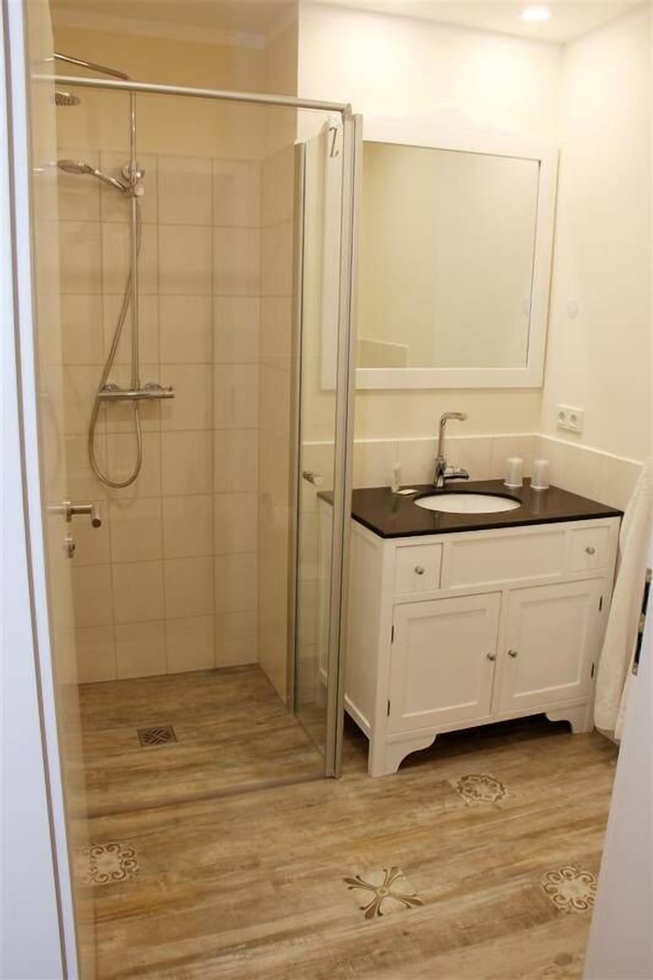 A bathroom with a glass-enclosed shower, a white sink with a black countertop, and a mirror above the sink.