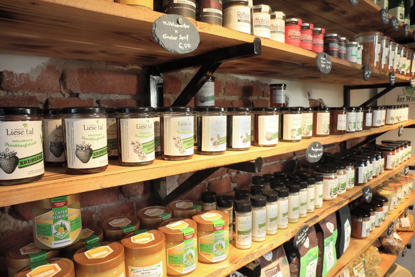A variety of food products on wooden shelves, including jars of preserves and honey.