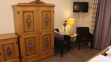 Une chambre d’hôtel avec une armoire en bois, un téléviseur fixé au mur, une petite table ronde avec une lampe, deux chaises et un lit.