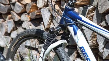 Una bicicleta de montaña con estructura blanca y detalles azules, apoyada contra un montón de troncos.