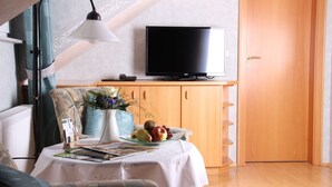 A room with a bed, a table with a magazine, a vase with flowers, a fruit bowl, a television on a stand, and a wooden cabinet. - Landidyll Landaus Liesetal (Hallenberg)
