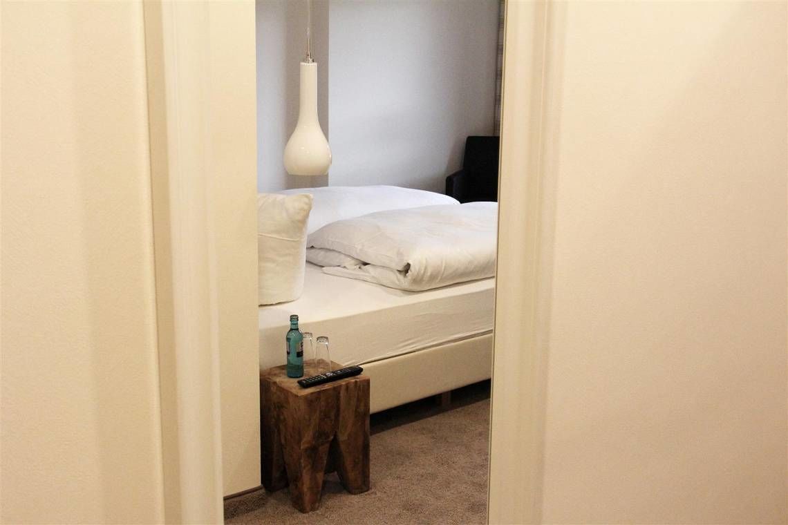 A bedroom with a bed, a bedside table, a remote control, and a bottle.