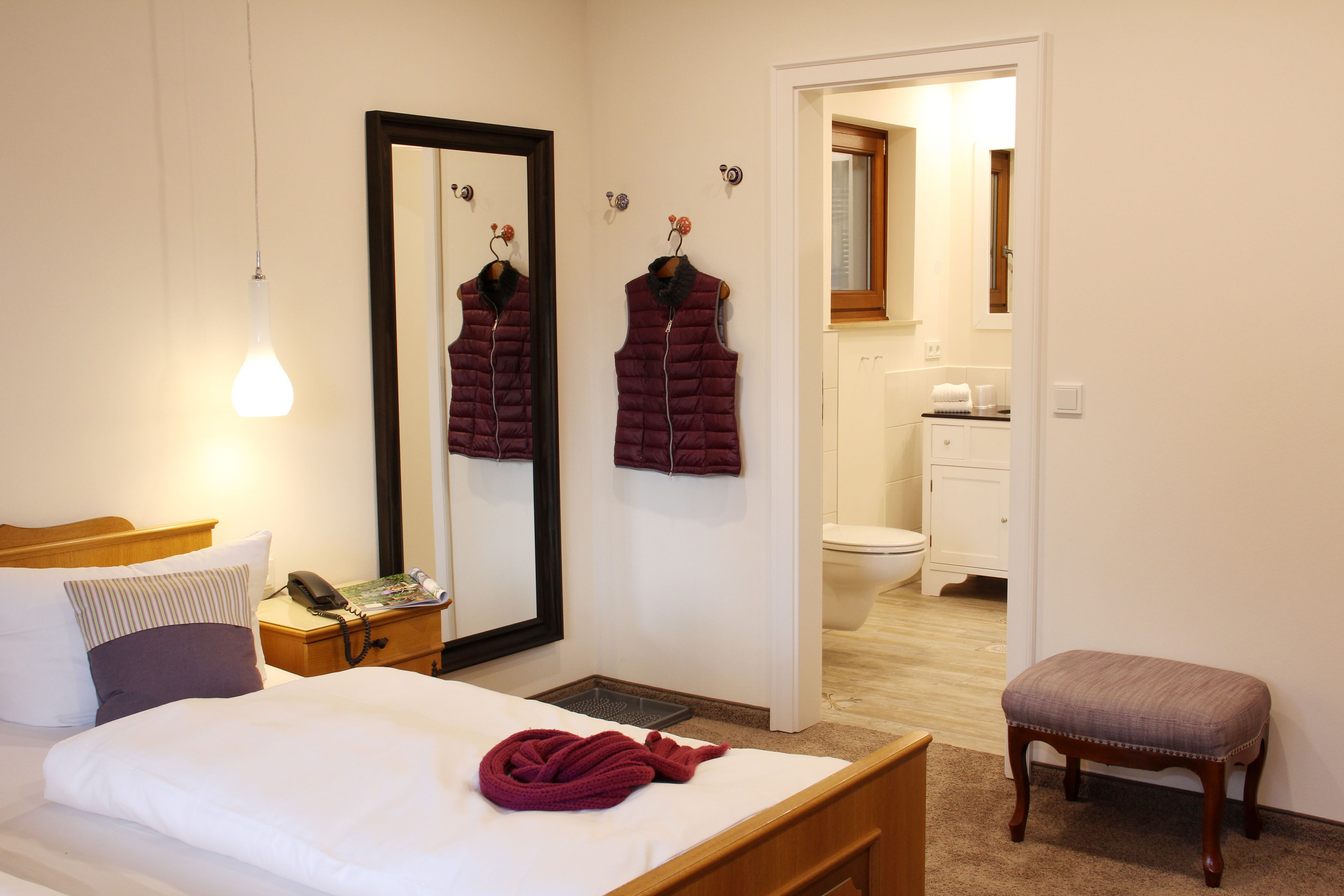 A hotel room with a bed, a bedside table with a phone, a mirror, and a bathroom visible through an open door.