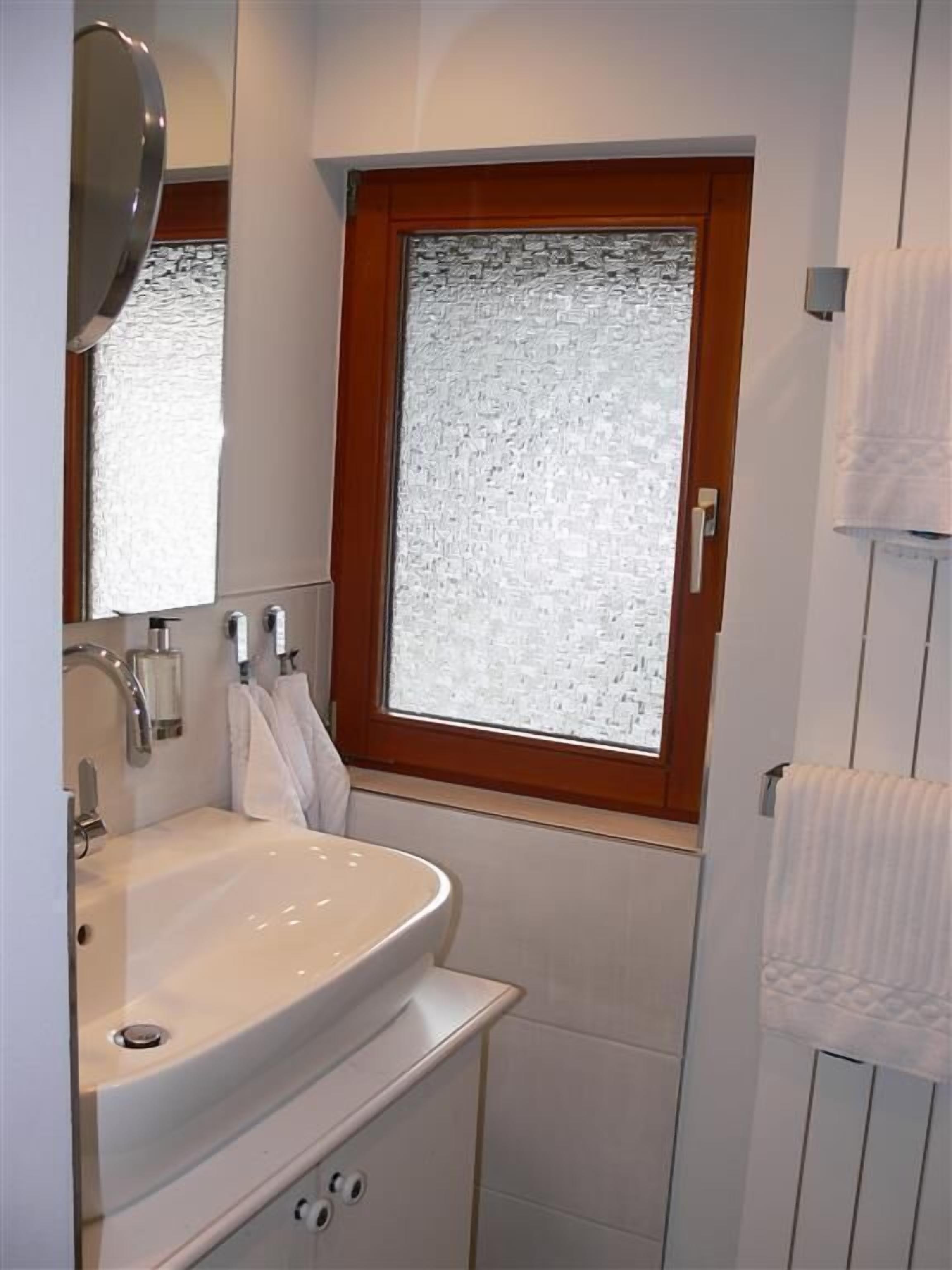 A bathroom with a white sink, a mirror, and a window with frosted glass.