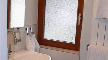 A bathroom with a white sink, a mirror, and a window with frosted glass.