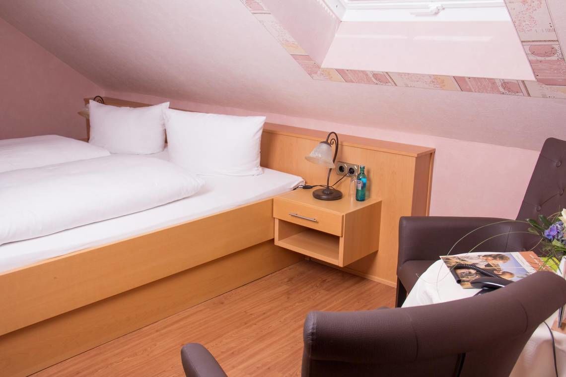 A small, cozy room with a bed, a desk, a chair, and a skylight.